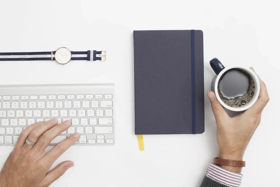Keyboard, notebook and coffee on a white desk