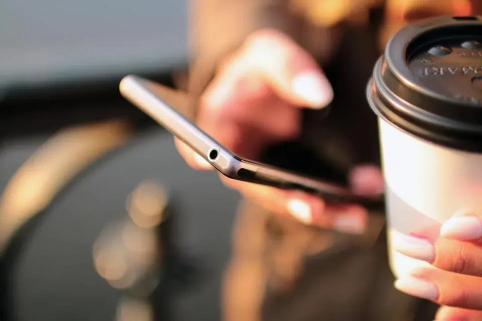 Hands holding a smartphone beside a coffee cup